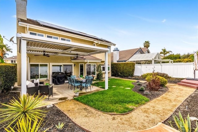 rear view of property featuring a patio, stucco siding, a ceiling fan, roof mounted solar panels, and fence