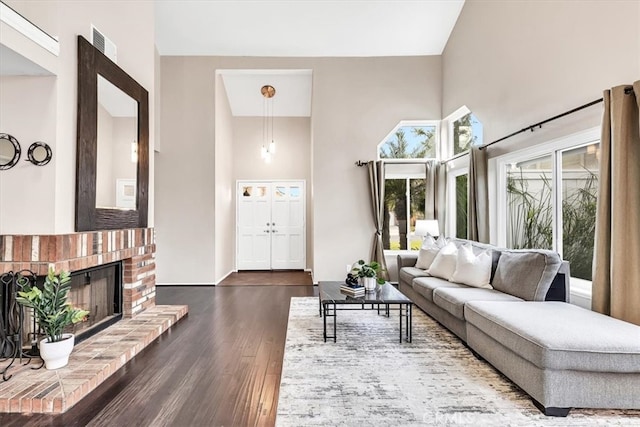 living area with visible vents, dark wood-type flooring, a fireplace, and a high ceiling