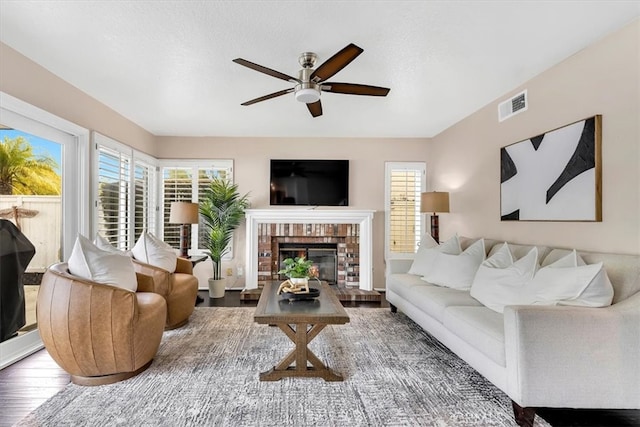 living area with a fireplace, wood finished floors, visible vents, and a ceiling fan