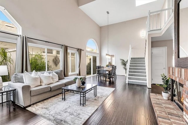 living room with dark wood-style flooring, stairway, a brick fireplace, and a towering ceiling