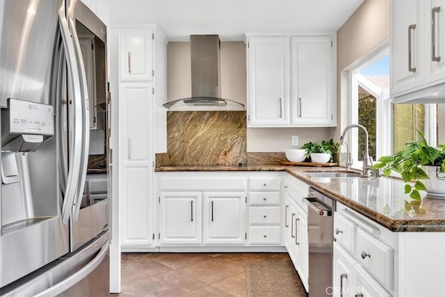 kitchen with wall chimney range hood, white cabinetry, appliances with stainless steel finishes, and a sink