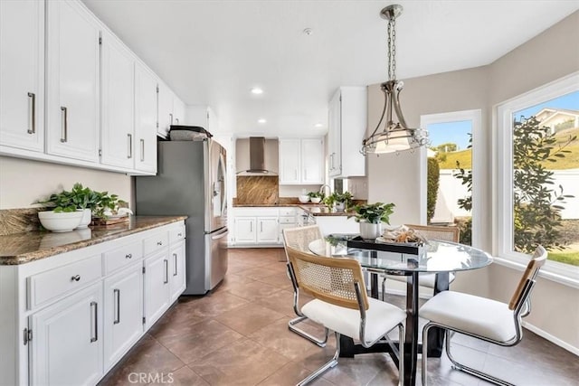 kitchen with a healthy amount of sunlight, wall chimney range hood, white cabinetry, and freestanding refrigerator