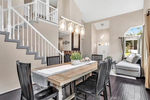 dining area with a towering ceiling, stairway, and dark wood finished floors