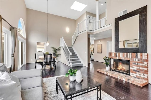 living area with a skylight, stairway, a brick fireplace, and wood finished floors