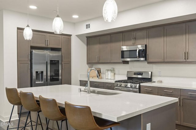 kitchen with a breakfast bar area, stainless steel appliances, a sink, visible vents, and hanging light fixtures