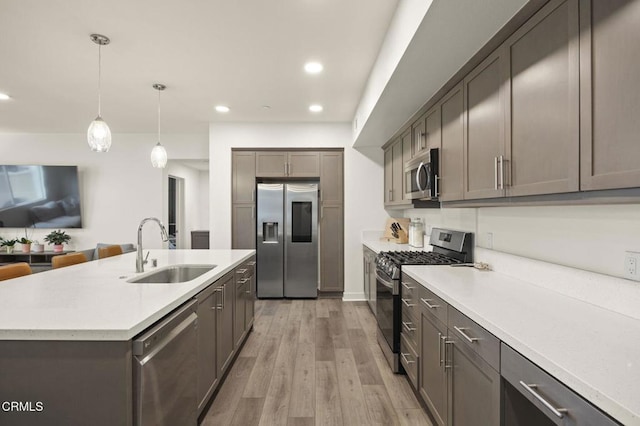 kitchen with recessed lighting, light countertops, light wood-style flooring, appliances with stainless steel finishes, and a sink