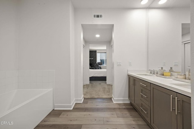 ensuite bathroom with connected bathroom, wood finished floors, a sink, visible vents, and a bath