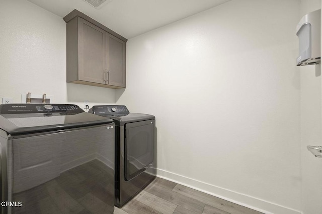 laundry area featuring cabinet space, visible vents, washing machine and dryer, wood finished floors, and baseboards