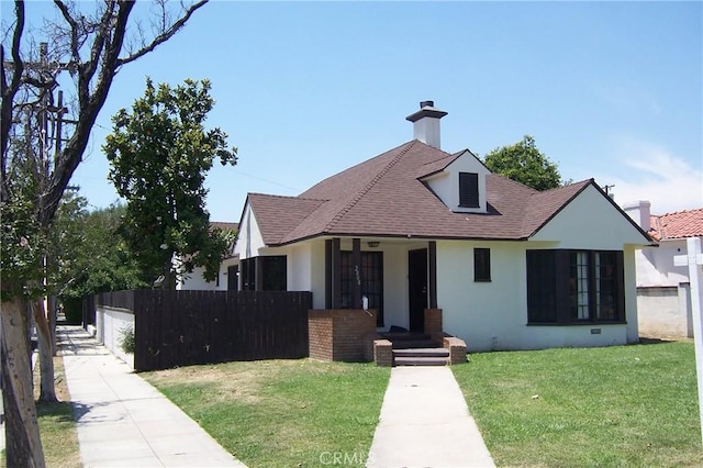 bungalow-style home with stucco siding, roof with shingles, fence, and a front yard