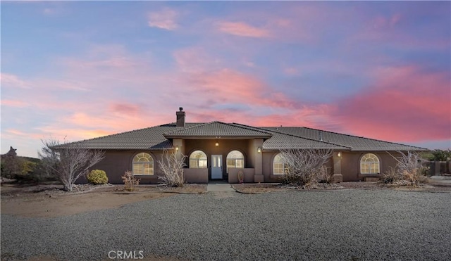 view of front of property featuring stucco siding, a chimney, and a tiled roof