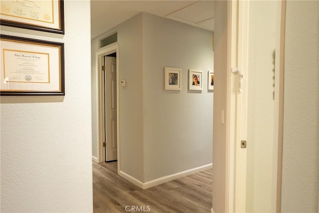 hallway with wood finished floors, visible vents, and baseboards