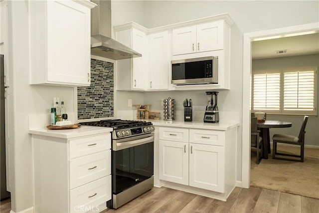 kitchen with stainless steel appliances, wall chimney exhaust hood, light countertops, and light wood-style flooring