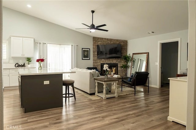 living area with visible vents, ceiling fan, light wood-style flooring, vaulted ceiling, and a fireplace