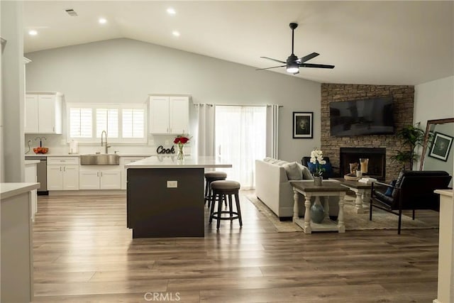 kitchen featuring a breakfast bar area, open floor plan, wood finished floors, a stone fireplace, and a sink