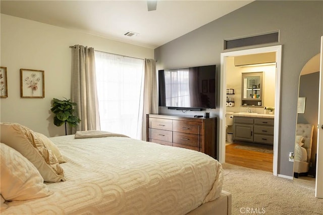 bedroom with arched walkways, light colored carpet, ensuite bathroom, vaulted ceiling, and a sink