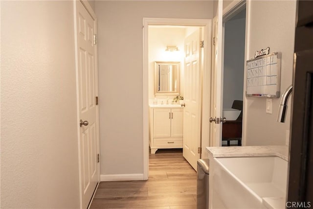 corridor featuring a sink, light wood-style flooring, and baseboards