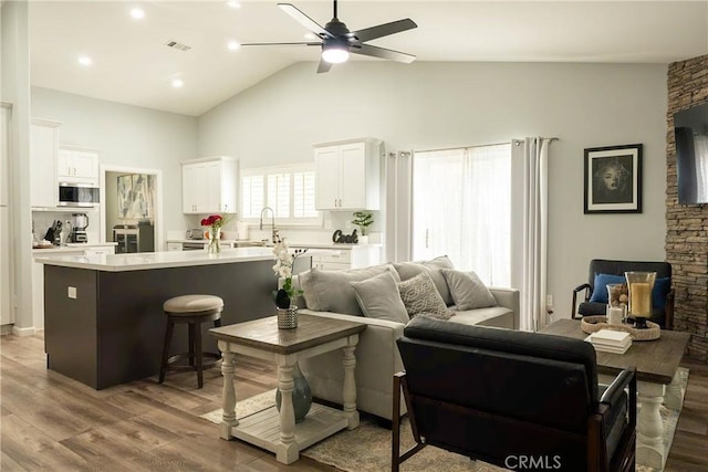 living area featuring high vaulted ceiling, ceiling fan, visible vents, and wood finished floors