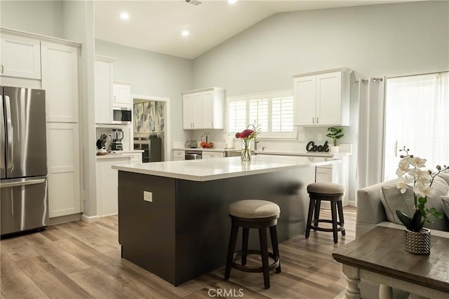 kitchen with white cabinets, a kitchen island, wood finished floors, stainless steel appliances, and a kitchen bar