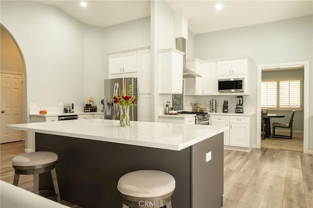 kitchen with arched walkways, light wood-style flooring, appliances with stainless steel finishes, white cabinets, and a kitchen bar