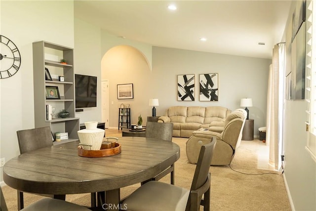 dining space featuring arched walkways, recessed lighting, light carpet, baseboards, and vaulted ceiling