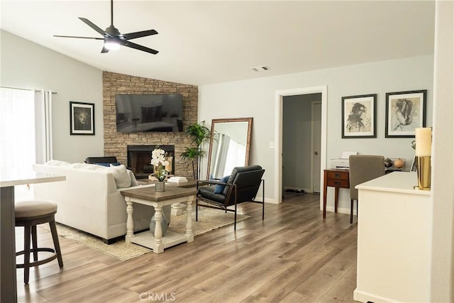 living area featuring a fireplace, visible vents, light wood-style flooring, vaulted ceiling, and ceiling fan