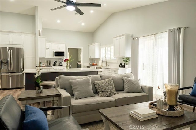 living room featuring ceiling fan, high vaulted ceiling, light wood-style flooring, and recessed lighting