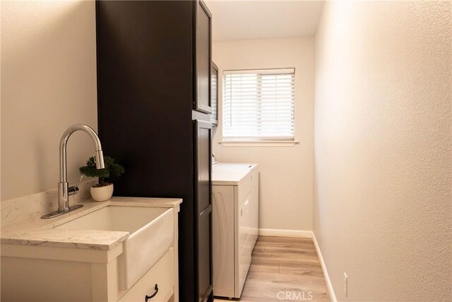 laundry room with laundry area, light wood finished floors, baseboards, washing machine and clothes dryer, and a sink