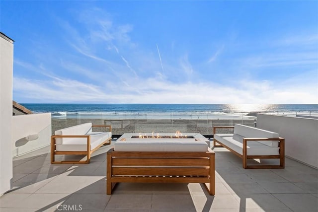 view of patio / terrace featuring an outdoor living space with a fire pit, a water view, and a beach view