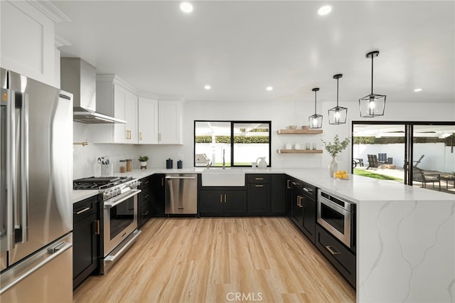 kitchen featuring stainless steel appliances, dark cabinetry, a sink, and wall chimney exhaust hood