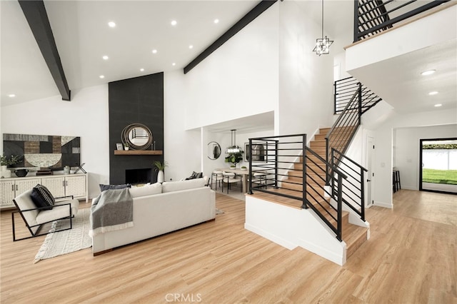 living room with a large fireplace, stairs, wood finished floors, and beam ceiling