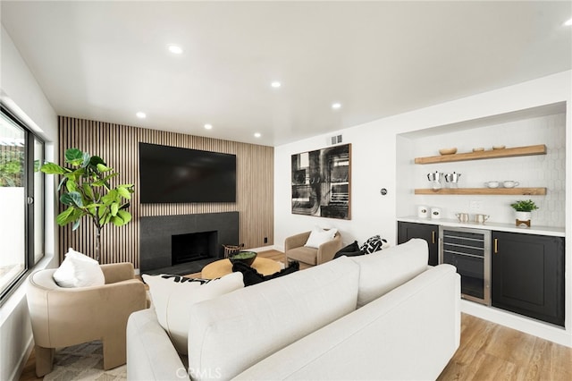 living area with wine cooler, light wood-style flooring, recessed lighting, a fireplace, and a bar