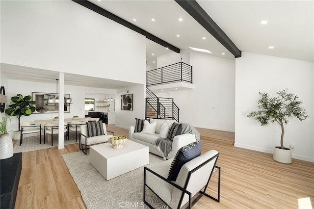 living area featuring high vaulted ceiling, light wood-style flooring, baseboards, stairs, and beamed ceiling