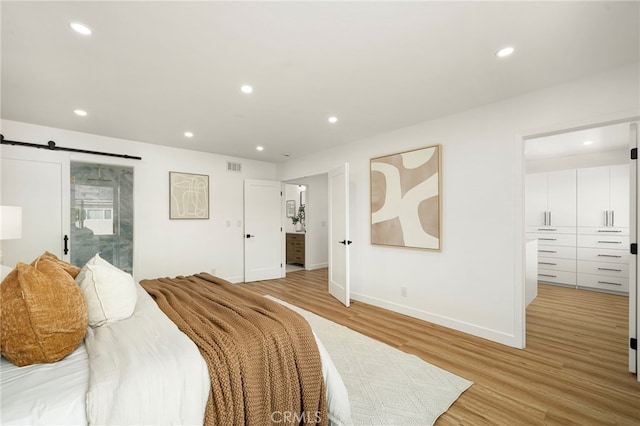 bedroom with a barn door, baseboards, light wood-style flooring, ensuite bathroom, and recessed lighting