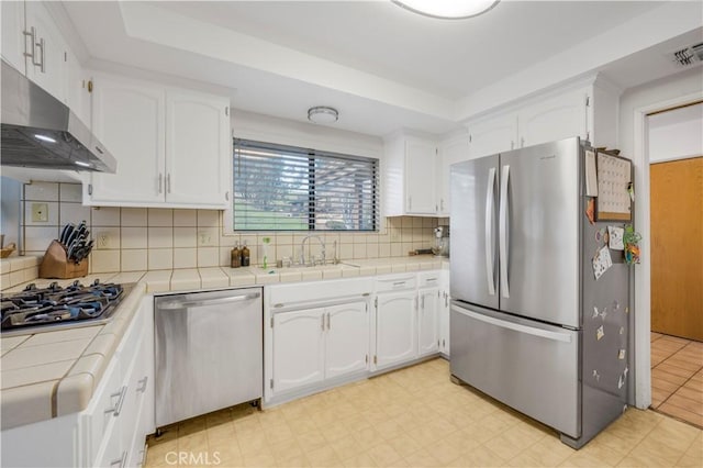 kitchen with under cabinet range hood, tile counters, appliances with stainless steel finishes, and a sink