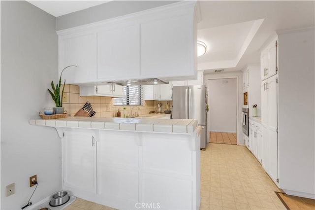 kitchen featuring tile countertops, a peninsula, white cabinetry, appliances with stainless steel finishes, and decorative backsplash