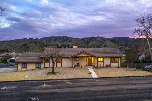 view of front of house featuring a chimney, fence, a mountain view, and stucco siding