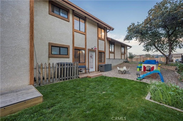 rear view of property with a yard, fence, and stucco siding