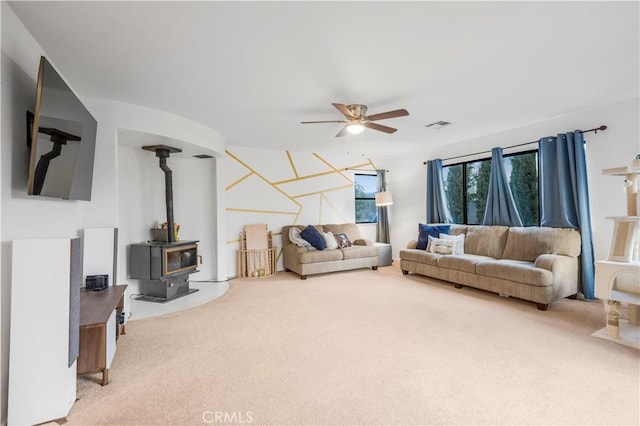 carpeted living area with a wood stove, visible vents, and ceiling fan