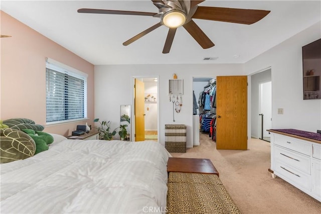 bedroom with ensuite bathroom, light colored carpet, a ceiling fan, visible vents, and a spacious closet