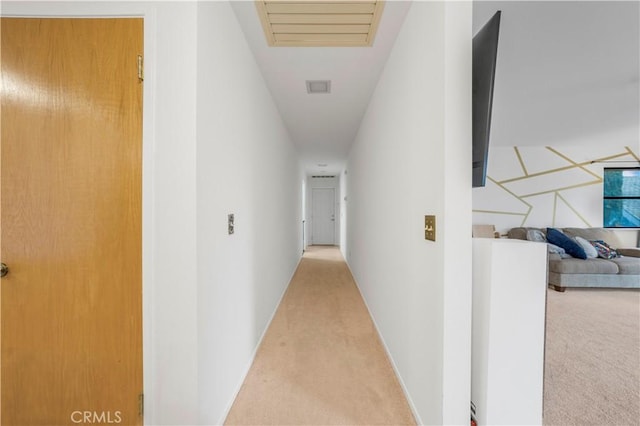 hallway with baseboards, visible vents, and light colored carpet