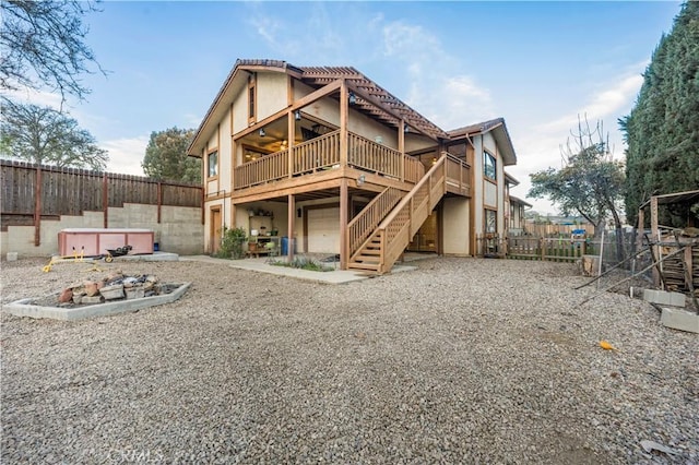 back of house with stucco siding, a hot tub, a deck, a fenced backyard, and stairs