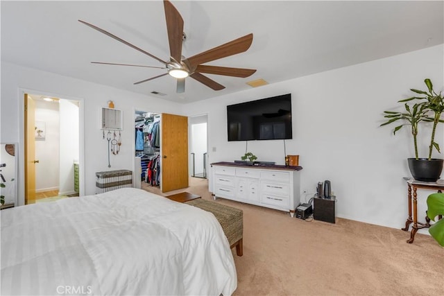 bedroom with visible vents, connected bathroom, light colored carpet, ceiling fan, and a walk in closet