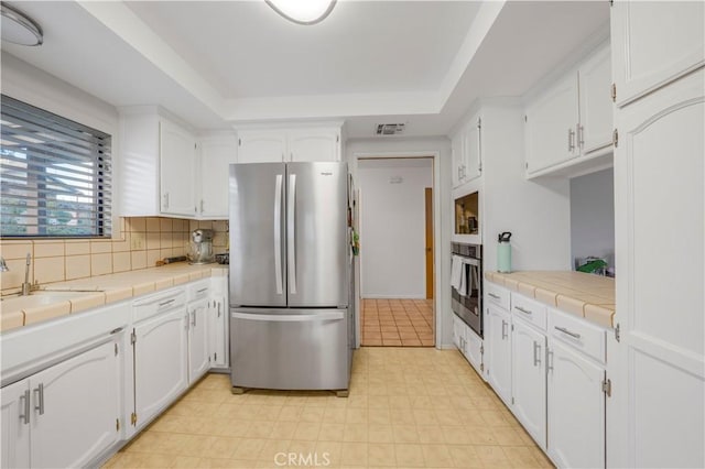 kitchen featuring tile counters, appliances with stainless steel finishes, a tray ceiling, white cabinetry, and a sink