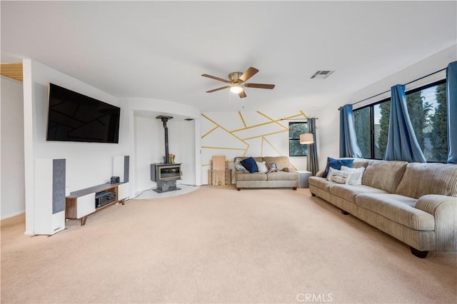 carpeted living room featuring a ceiling fan, a wood stove, and visible vents