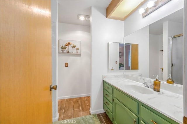 full bathroom featuring a shower with door, wood tiled floor, baseboards, and vanity