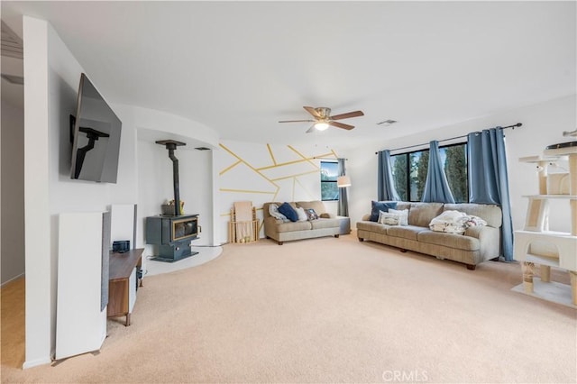 living room featuring ceiling fan, carpet floors, visible vents, and a wood stove