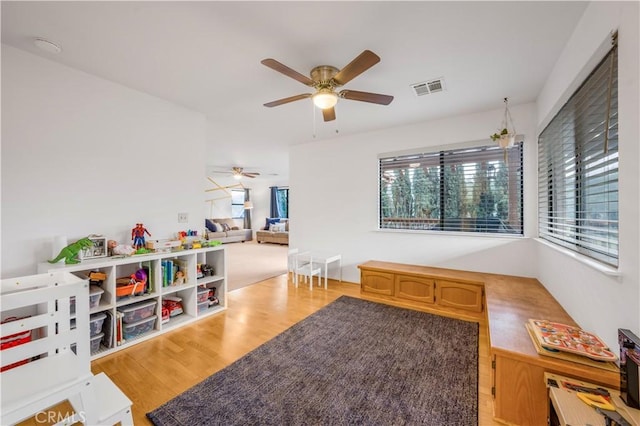 playroom with light wood-style floors, a healthy amount of sunlight, visible vents, and ceiling fan