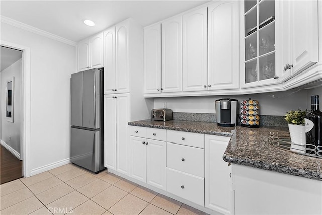 kitchen featuring dark stone countertops, white cabinetry, freestanding refrigerator, light tile patterned floors, and glass insert cabinets