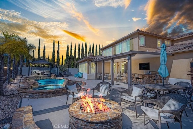 patio terrace at dusk featuring fence, a fire pit, a fenced in pool, and an in ground hot tub