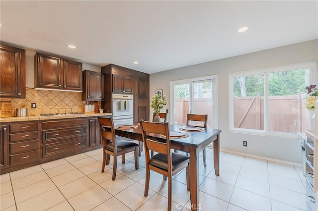 kitchen featuring tile countertops, gas stovetop, backsplash, dark brown cabinets, and oven